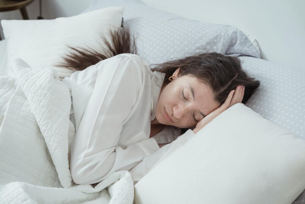 A young woman peacefully sleeping on her side in a white, minimal bedroom