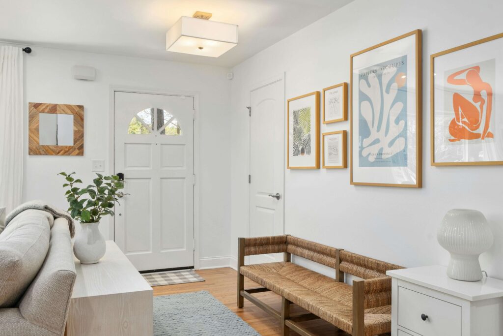 welcoming-entry-greenery A bright entryway with a front door opening to a calm, art-filled space with greenery and a welcoming bench.