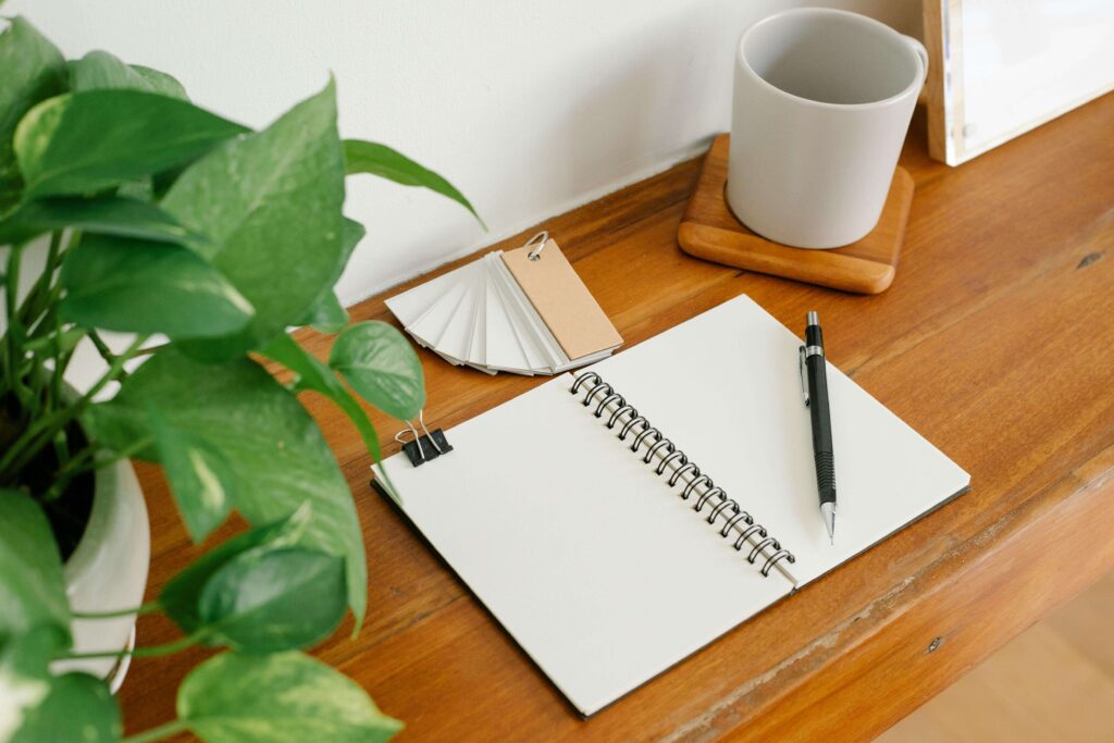 Broad-leaf plant beside a wood desk with notebook and neutral mug, calm home office feng shui
