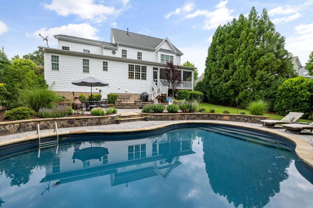 A backyard swimming pool with soft curved edges in front of a white house, symbolizing smoother energy flow in Feng Shui.