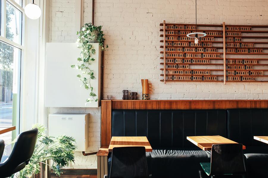 Cafe interior with wooden tables, black seating, and indoor plants by the window, creating a balanced and welcoming atmosphere