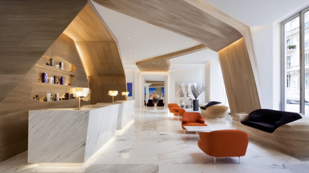 A modern hotel reception area with warm lighting, natural wood features, a sculptural marble front desk, and an open flowing lobby layout that creates a calm and welcoming arrival experience.
