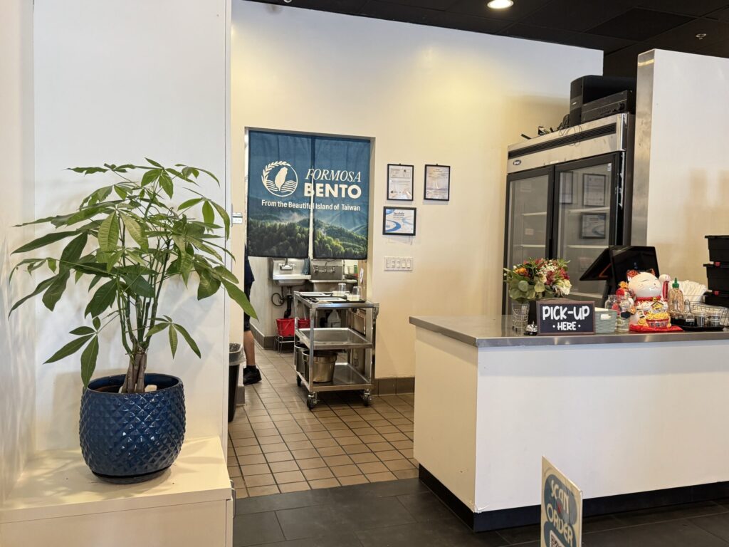 A small restaurant reception area with a green potted plant placed beside the counter, softening the space and stabilizing the energy flow in an otherwise simple layout.
