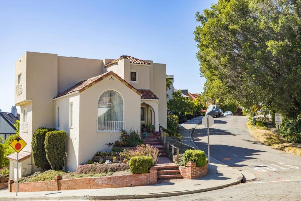 Street-level photo of a corner lot home with two street-facing sides along a curving road, showing high visibility and exposure.